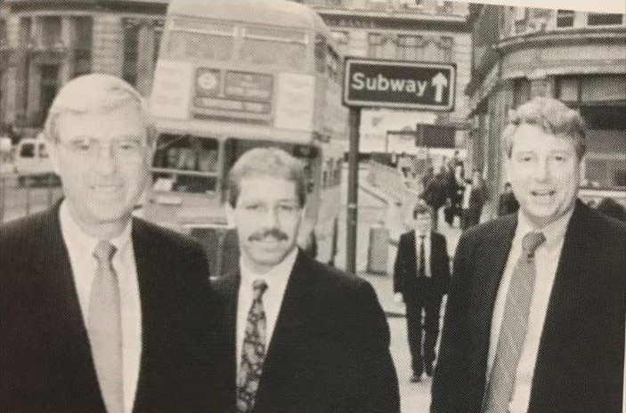 Black & white photo of Larry Lesser, Rich Boehne, and Dan Castellini out in the street wearing suits and ties