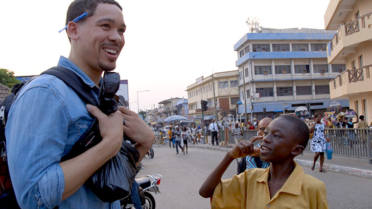 Photo of a journalist smiling as a young boy talks to him while he is on an assignment