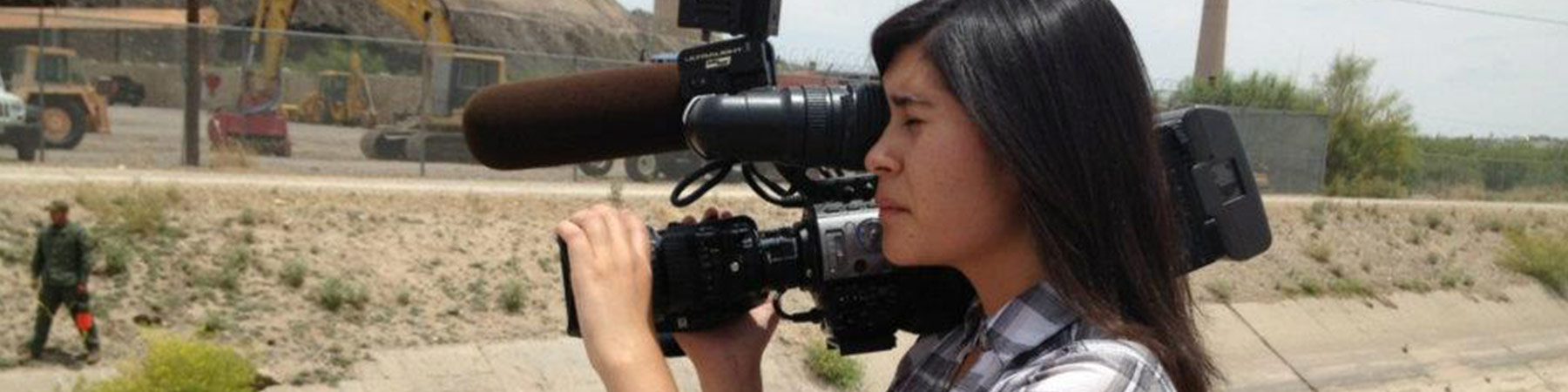 Photo of a camerawoman holding a video camera on her shoulder while looking through the lens