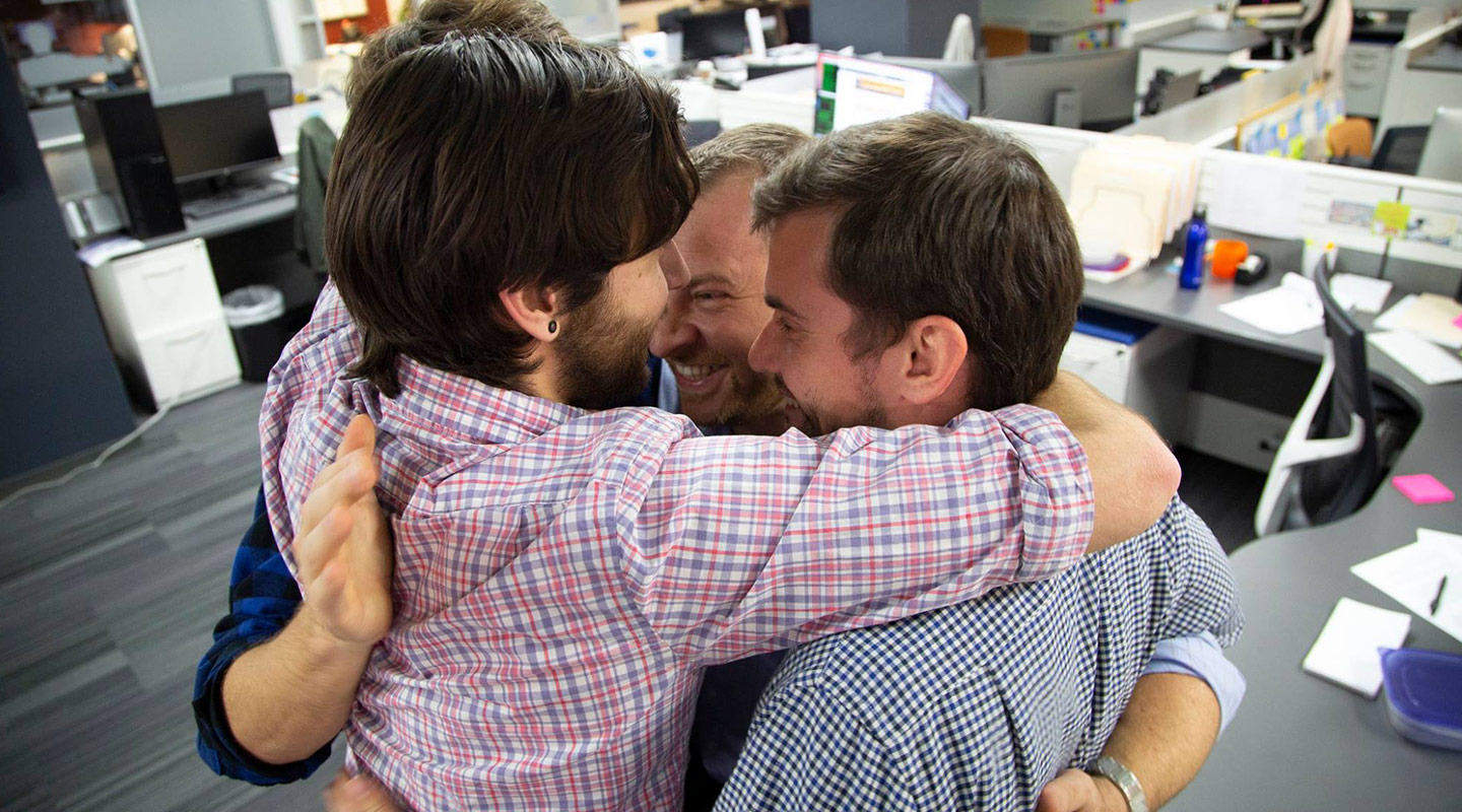 men hugging in a circle after receiving grant
