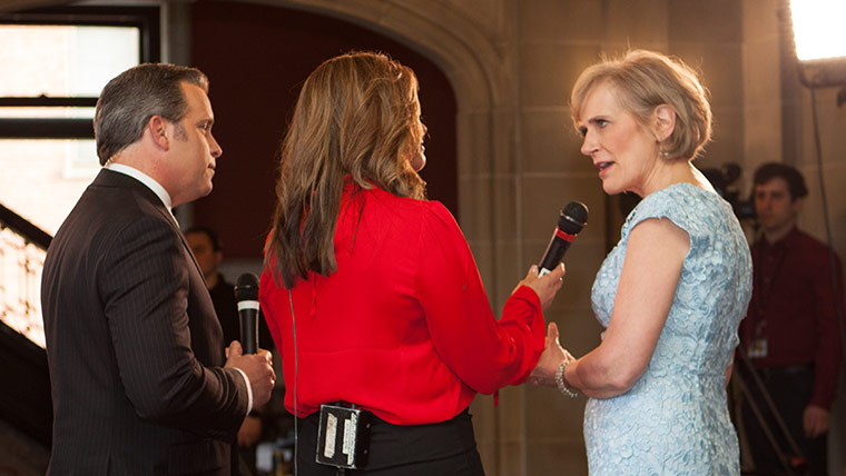 Photo of female news talent interviewing a woman as a man stands and listens