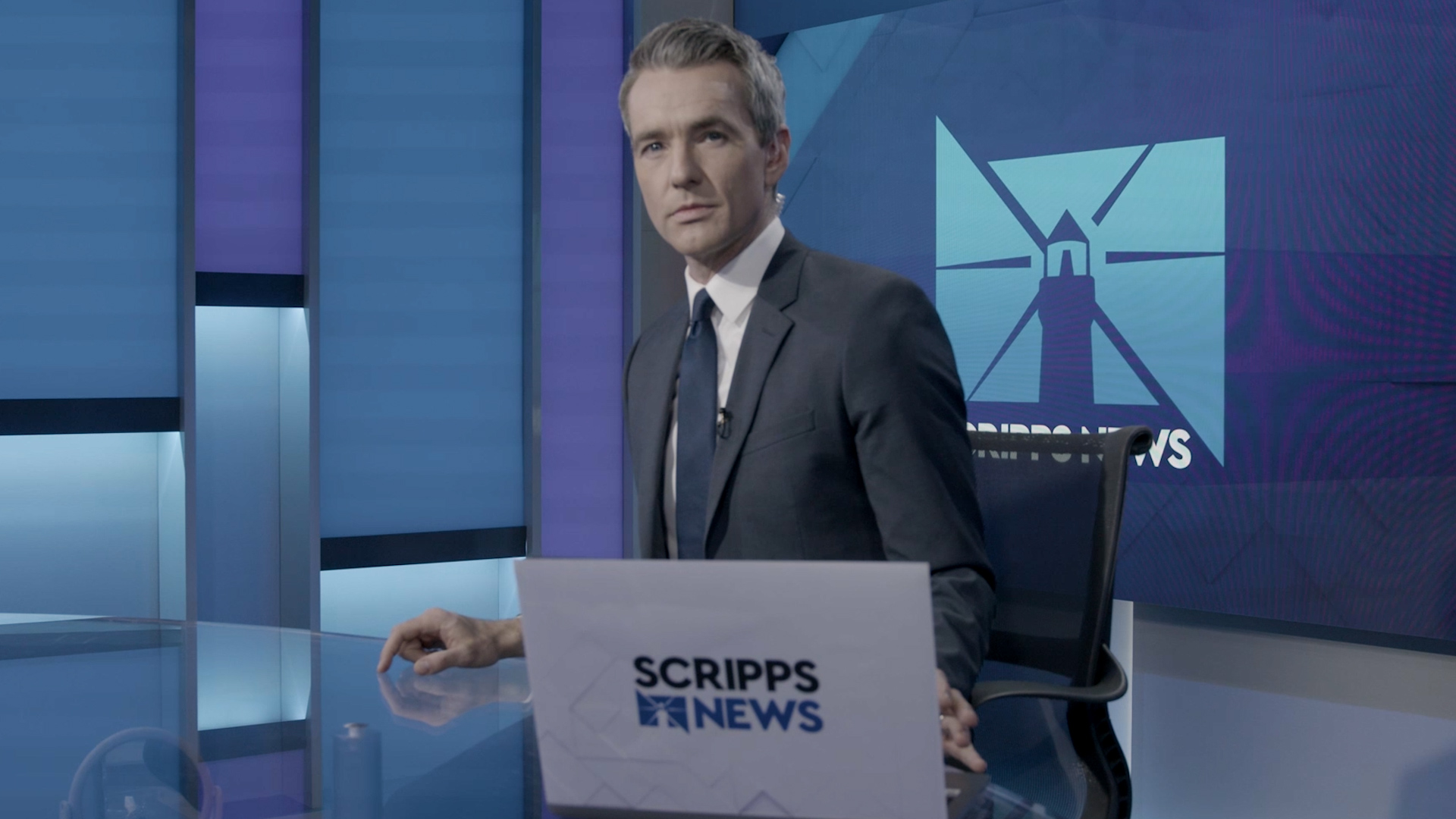 photo of a scripps news anchor in a grey suit, sitting in front of a blue background with the scripps news logo