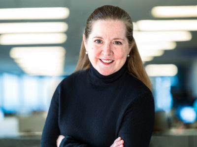 Photo of Kate O'Brian, Scripps News President, in a black turtleneck wearing peal earrings with her arms crossed