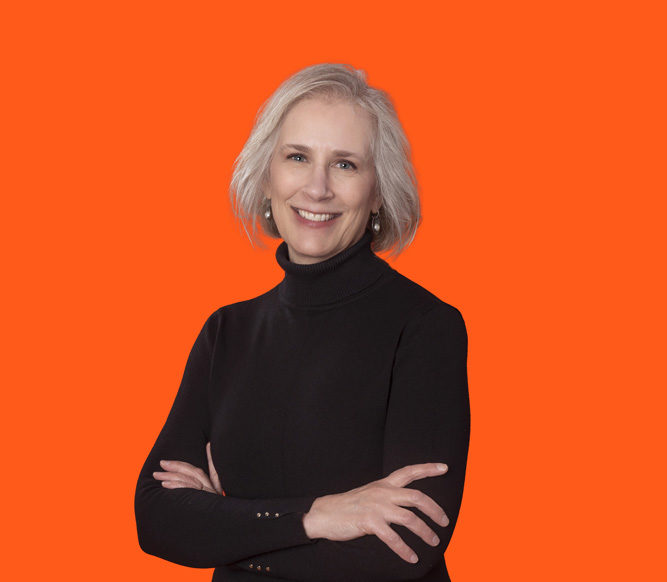 Headshot photo of Ms. Liz Carter with her arms crossed standing in front of an orange background