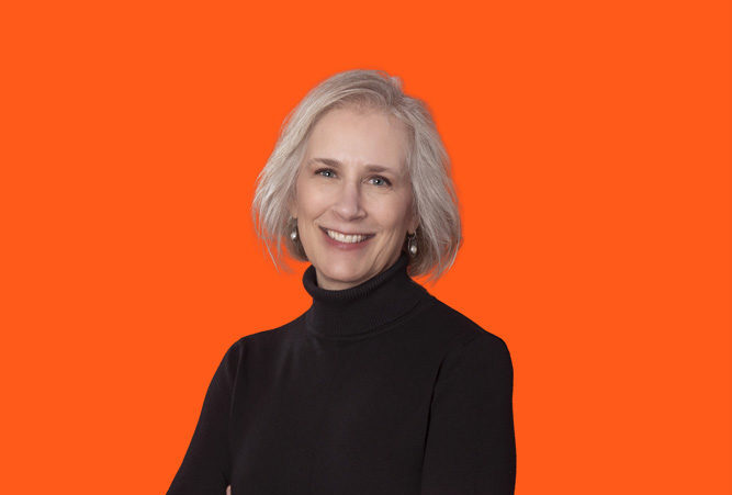 Headshot photo of Ms. Liz Carter with her arms crossed standing in front of an orange background