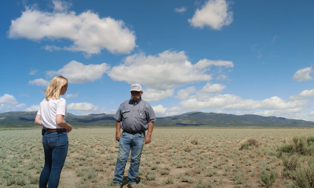A female reporter standing in an open field as she interviews a man about for an environmental documentary.