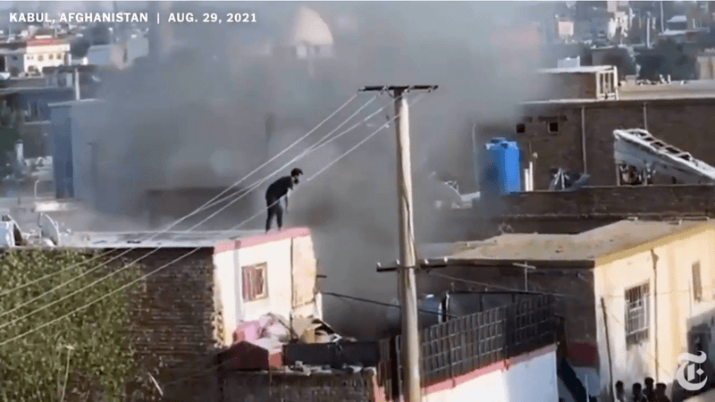 Photo of a man in black clothing standing on a roof as black smoke rises all around him in Afghanistan