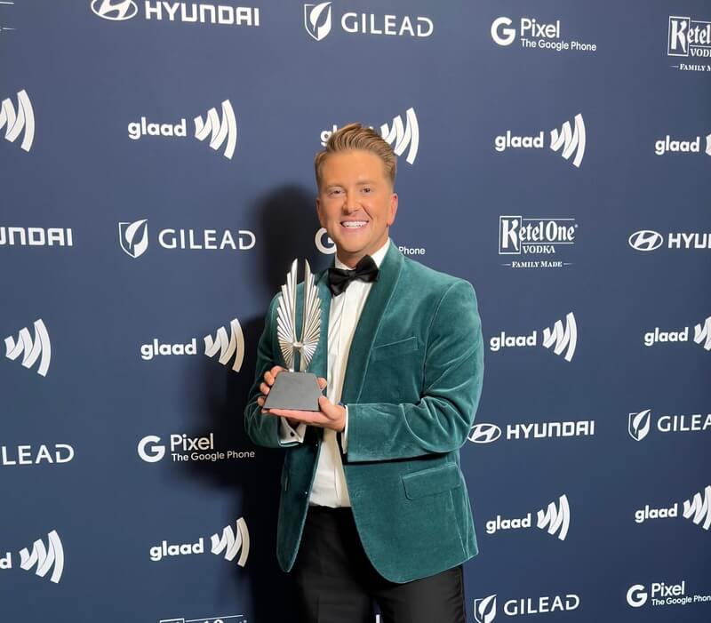 Photo of a man wearing a green suit jacket accepting a GLAAD award for outstanding TV journalism segment