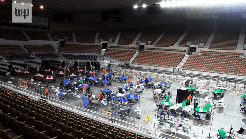 Photo of workers setting up a voting area in the center of an empty arena
