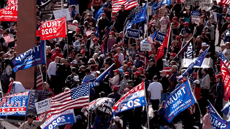 Photo of a huge crowd of people holding giant red and blue Trump 2020 campaign flags