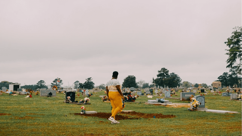 Photo of a woman walking by a recently filled grave in a graveyard