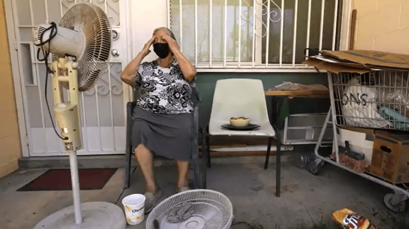 Photo of a woman sitting in a chair outside on a porch with a fan blowing on her