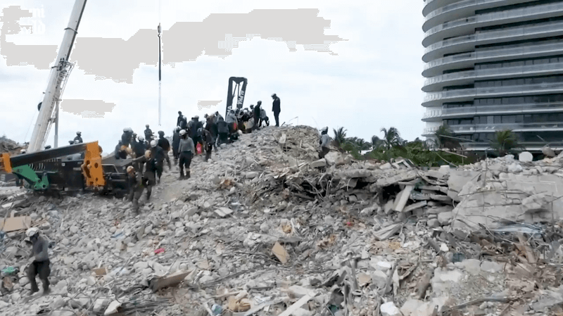Photo of construction workers standing on a huge pile of rubble by a crane