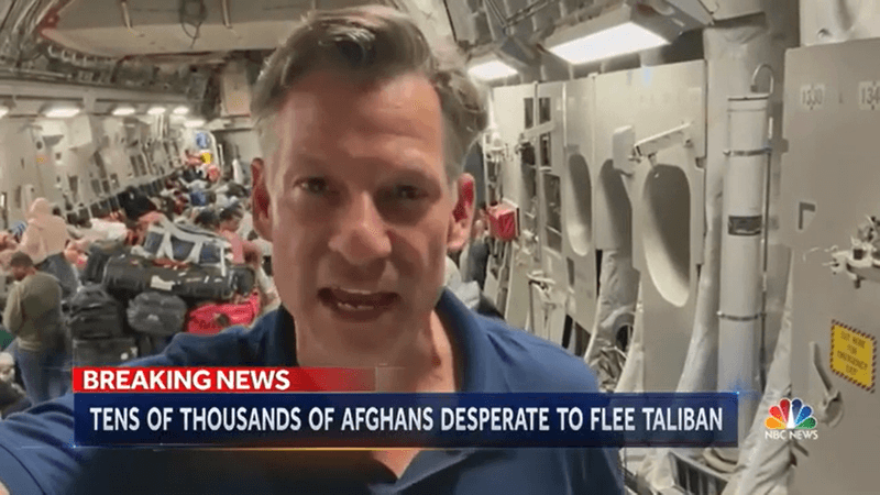 Photo of a news anchor inside of a plane surrounded by lots of bags