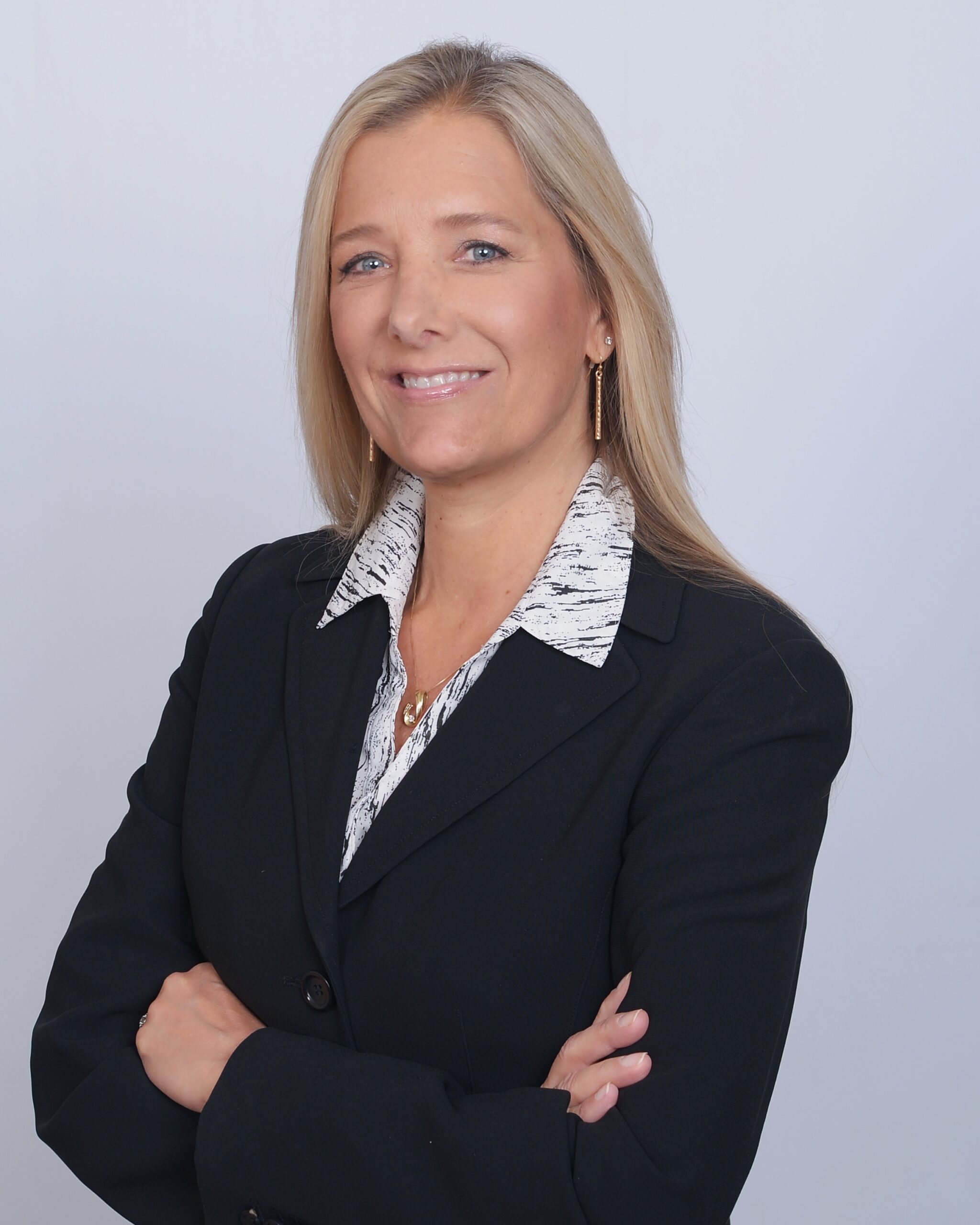 Woman with blonde hair in black suit jacket with arms folded.