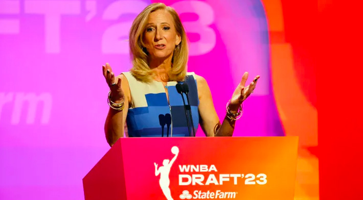 A woman at the WNBA draft podium is giving a speech.