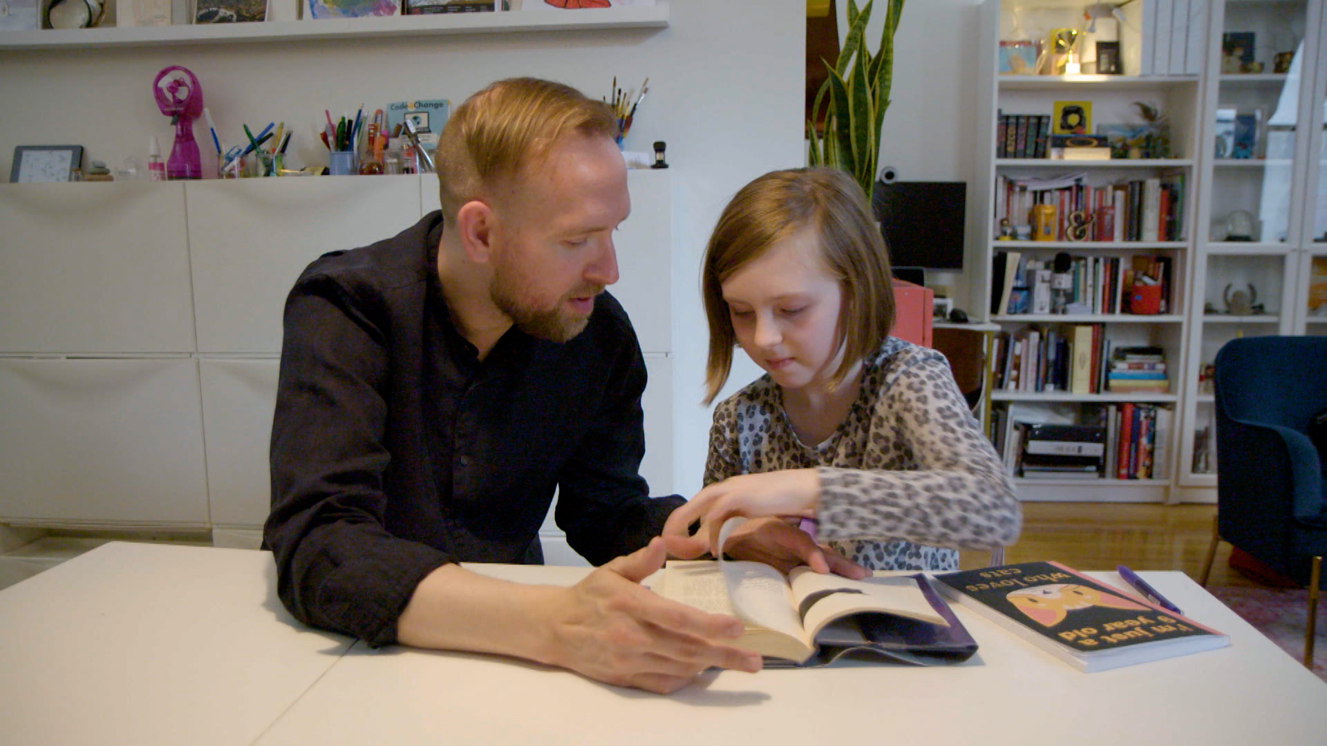A man and teaches a young girl how to read while at home.