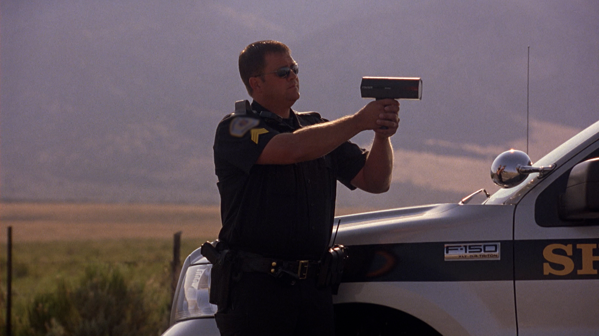 This is an image of a policeman holding a radar gun next to his vehicle.