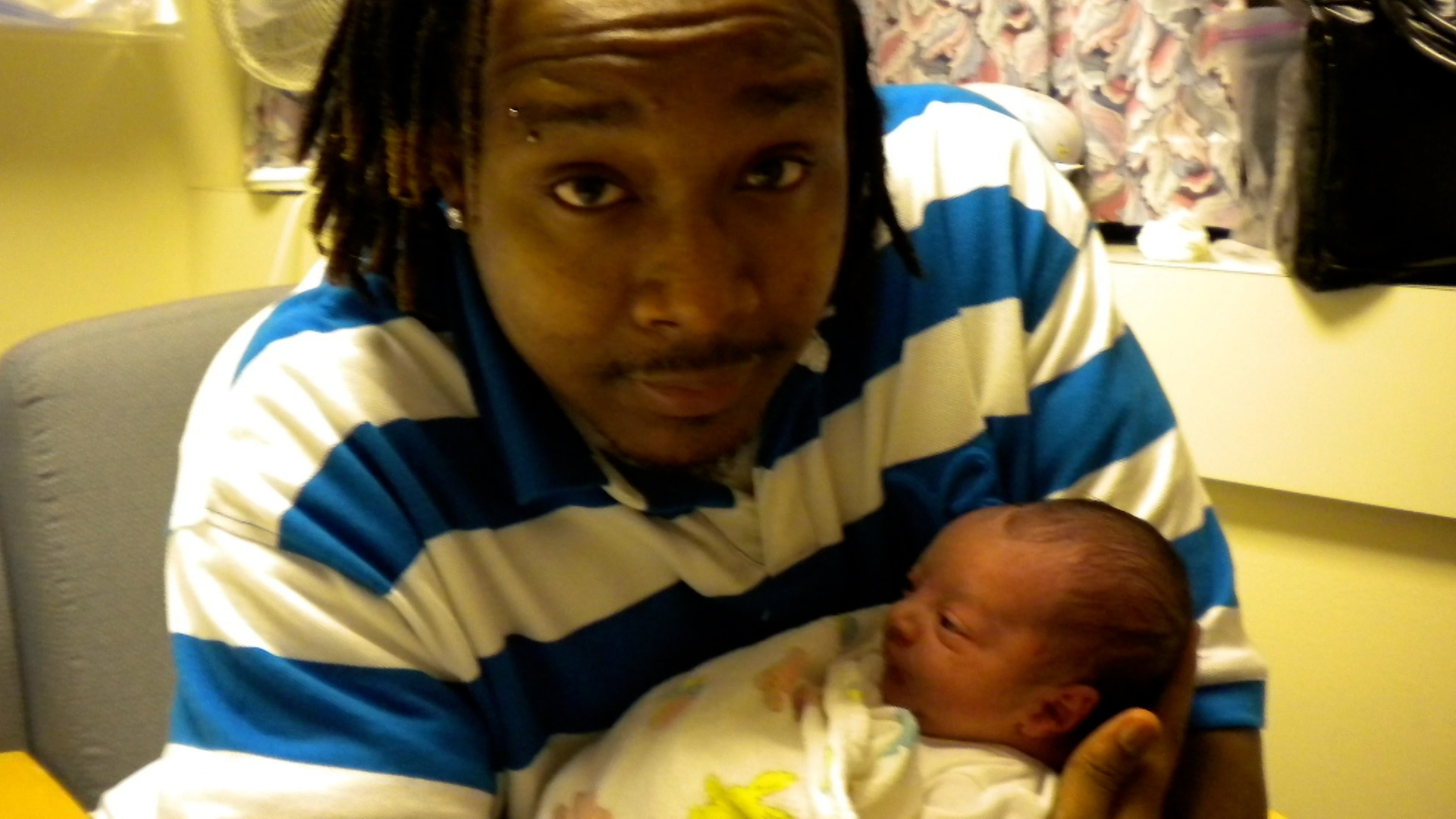 A young man in a stripped shirt holds his newborn child.