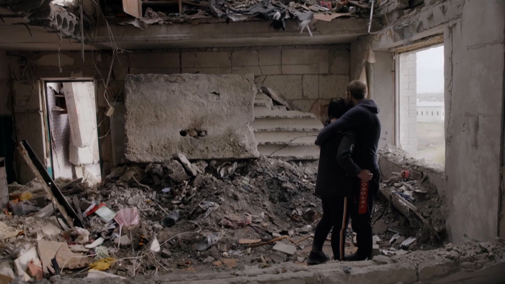 A man and woman comfort each other in the rubble of their home that was leveled in the Ukrainian war.