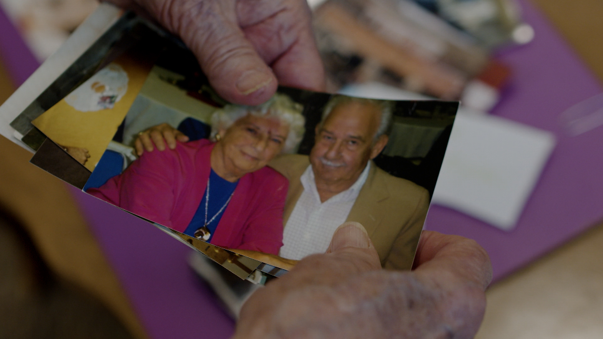 A pair of hands holds a photo of an elderly couple.